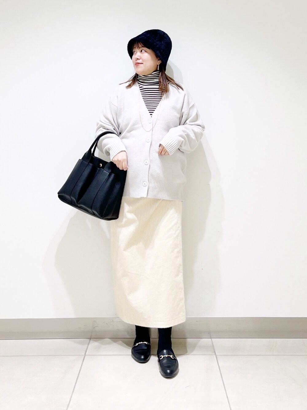 グレー系のニット/セーター、ホワイト系のカーディガン/ボレロ、ブラック系のトートバッグを着用したレディースの冬コーディネートの1枚目の写真
