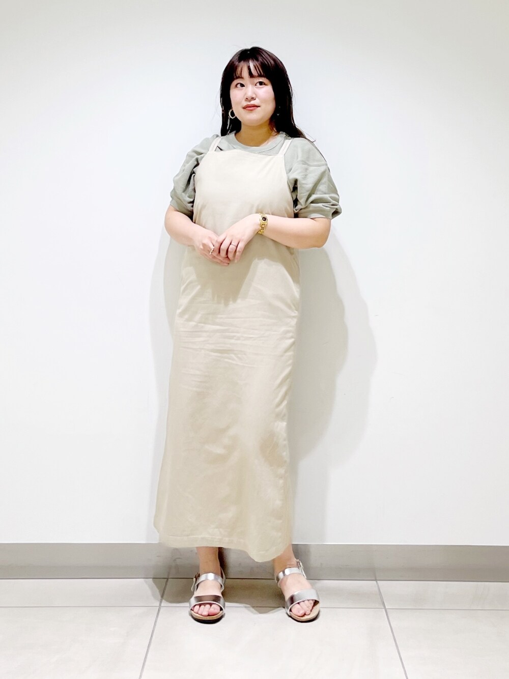 ベージュ系のワンピース、シルバー系のサンダル、グリーン系のTシャツ/カットソーを着用したレディースの春コーディネートの1枚目の写真