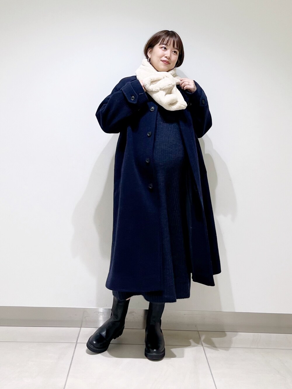 ブルー系のステンカラーコート、ブルー系のワンピース、ブラック系のブーツを着用したレディースの冬コーディネートの1枚目の写真