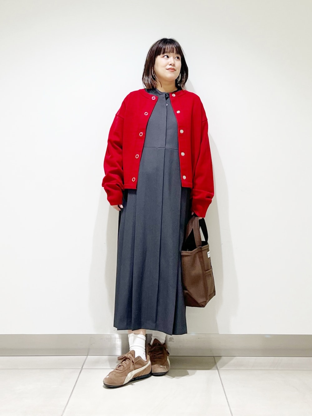 グレー系のワンピース、ブラウン系のトートバッグ、レッド系のカーディガン/ボレロを着用したレディースの秋コーディネートの1枚目の写真