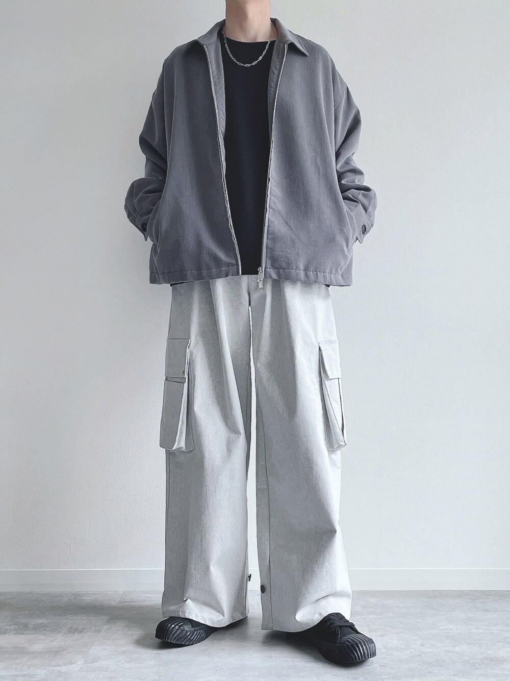 グレー系のブルゾン、ブラック系のトップス、ホワイト系のカーゴパンツを着用したメンズの春コーディネートの1枚目の写真