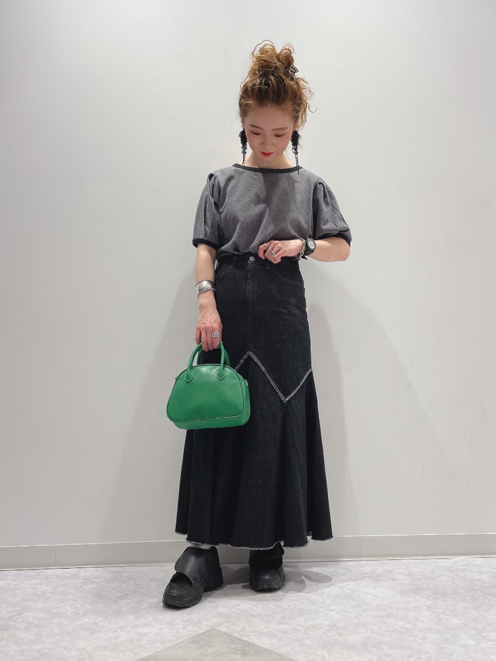 グリーン系のショルダーバッグ、ブラック系のデニムスカート、ブラック系のスニーカーを着用したレディースの夏コーディネートの1枚目の写真