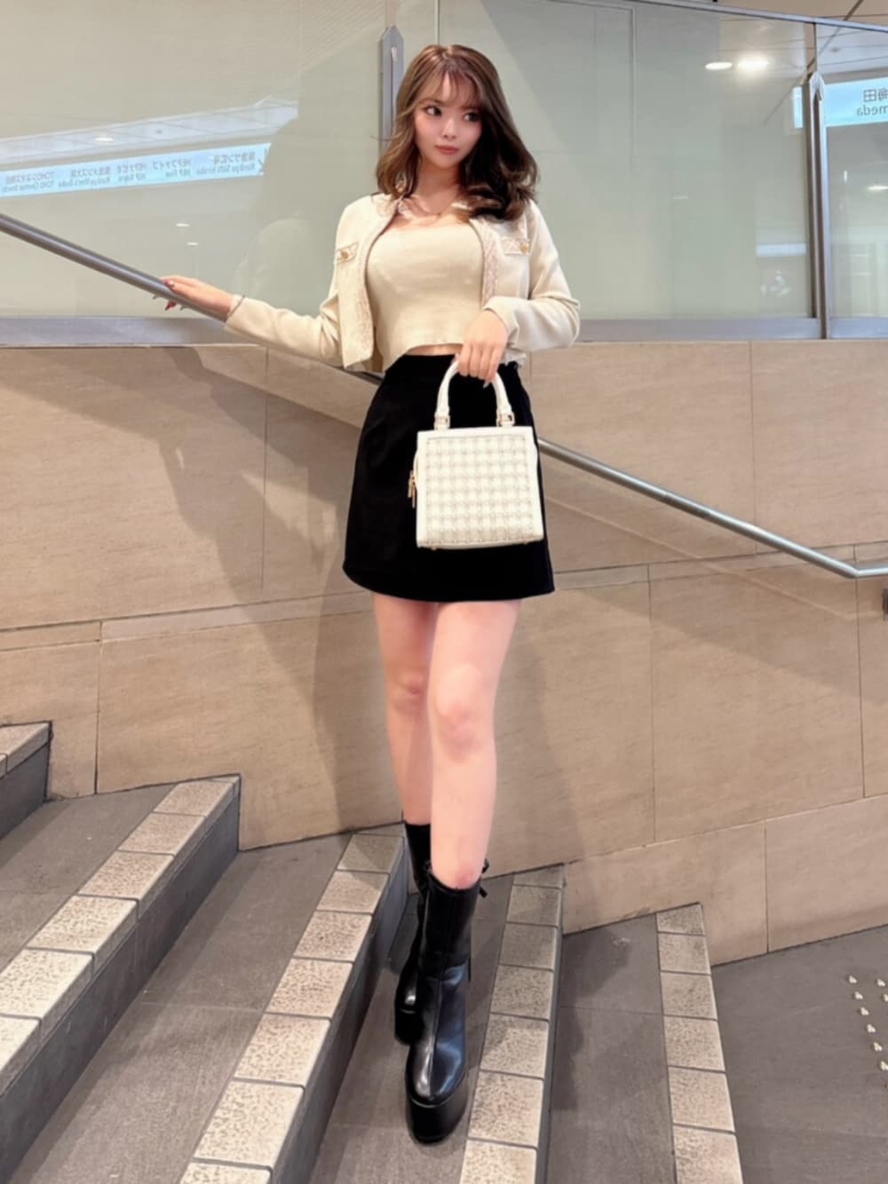 ブラック系のブーツ、ブラック系のスカート、ベージュ系のニット/セーターを着用したレディースの春コーディネートの1枚目の写真