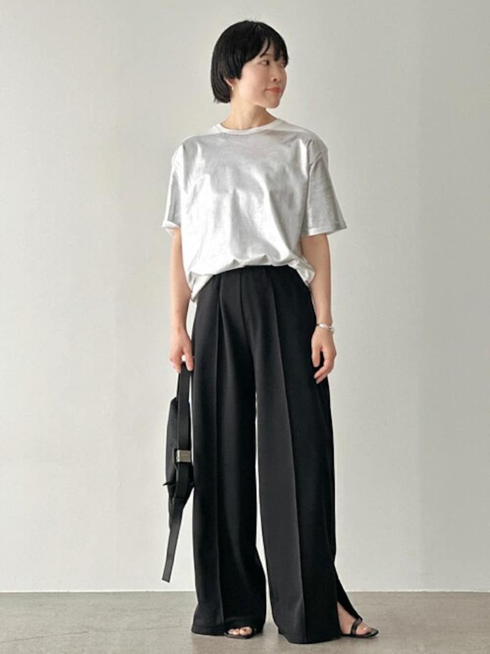 ブラック系のスラックス、ホワイト系のTシャツ/カットソー、ブラック系のサンダルを着用したレディースの春コーディネートの1枚目の写真