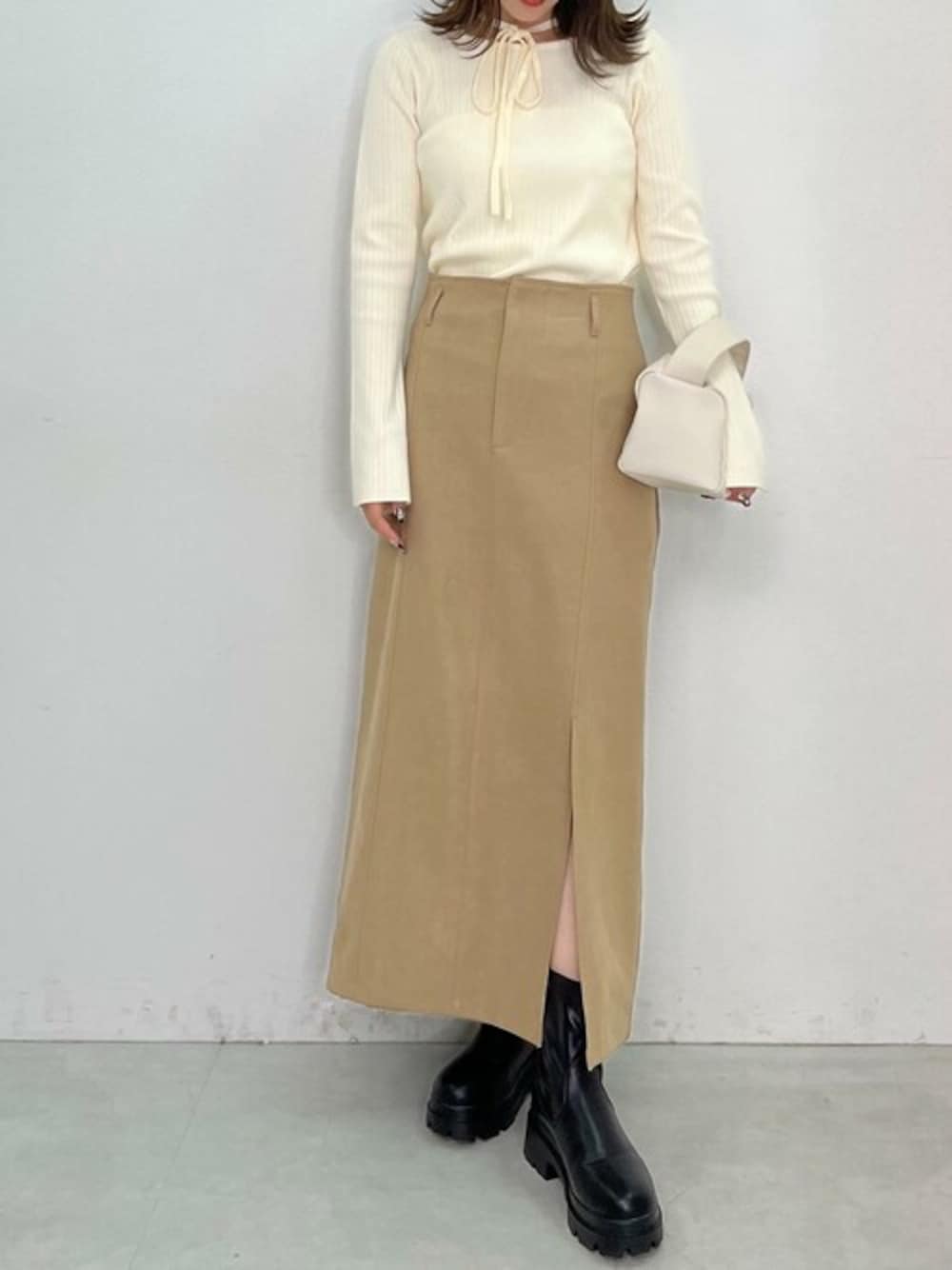 ホワイト系のニット/セーター、ベージュ系のスカート、ブラック系のブーツを着用したレディースの冬コーディネートの1枚目の写真