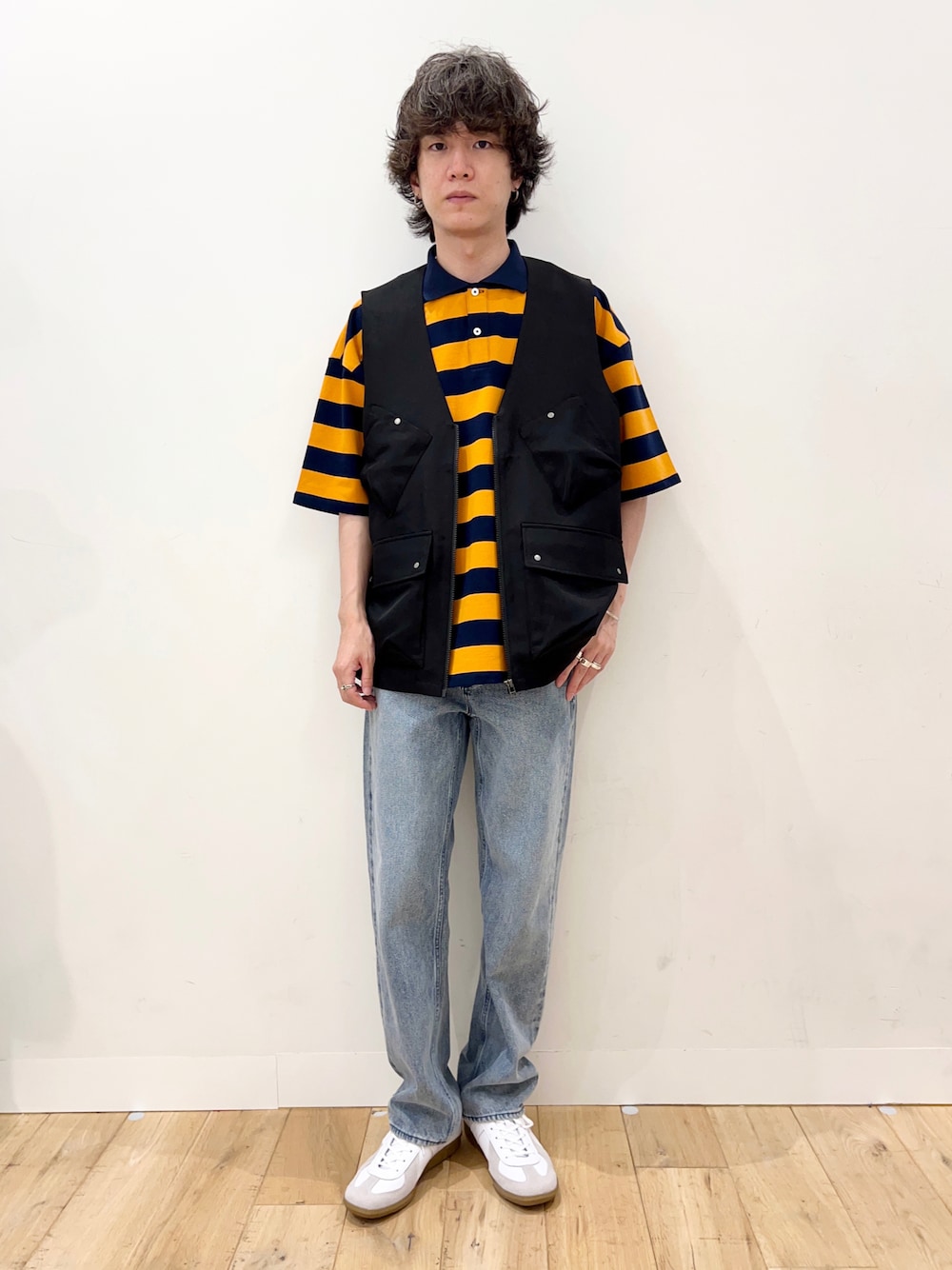 オレンジ系のポロシャツ、ブラック系のベスト、ブルー系のデニムパンツを着用したメンズの夏コーディネートの1枚目の写真