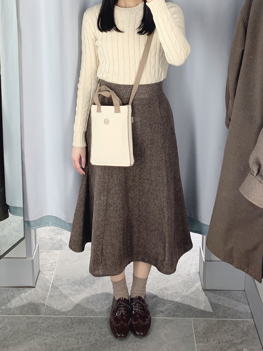 ホワイト系のニット/セーター、ブラウン系のスカート、ベージュ系のショルダーバッグを着用したレディースの冬コーディネートの1枚目の写真