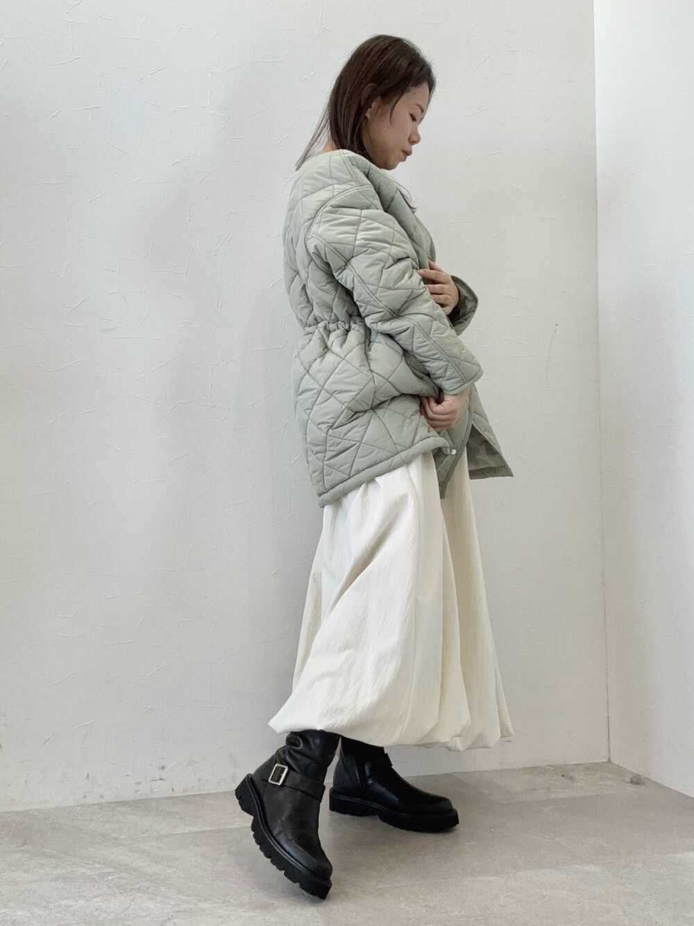 グリーン系のダウンジャケット/コート、ホワイト系のスカート、ブラック系のブーツを着用したレディースの冬コーディネートの1枚目の写真