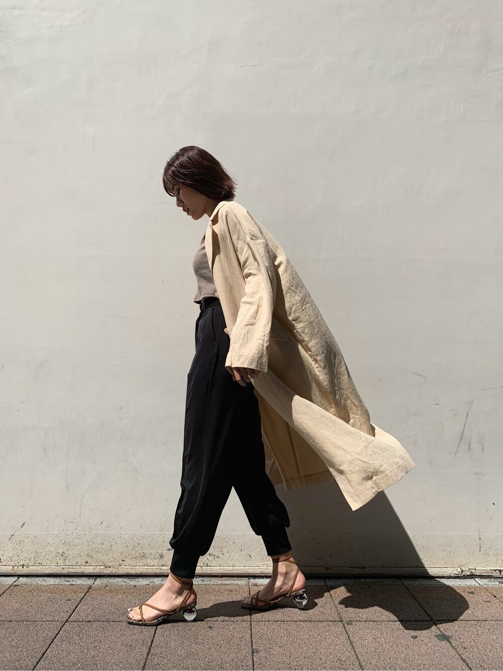 ベージュ系のチェスターコート、ブラック系のその他パンツ、ブラウン系のサンダルを着用したレディースの春コーディネートの1枚目の写真