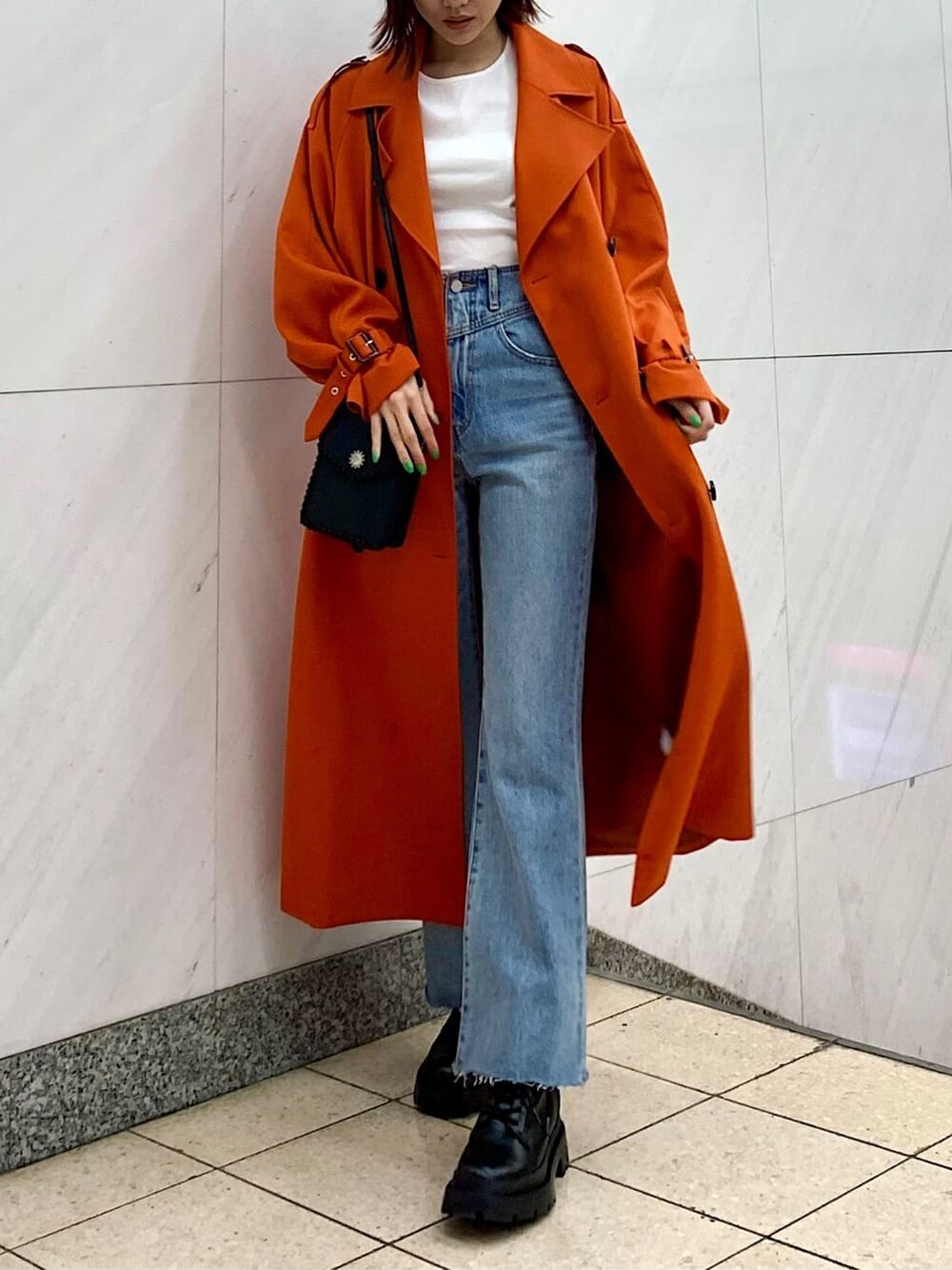 ブラック系のショルダーバッグ、オレンジ系のトレンチコート、ブルー系のデニムパンツを着用したレディースの冬コーディネートの1枚目の写真