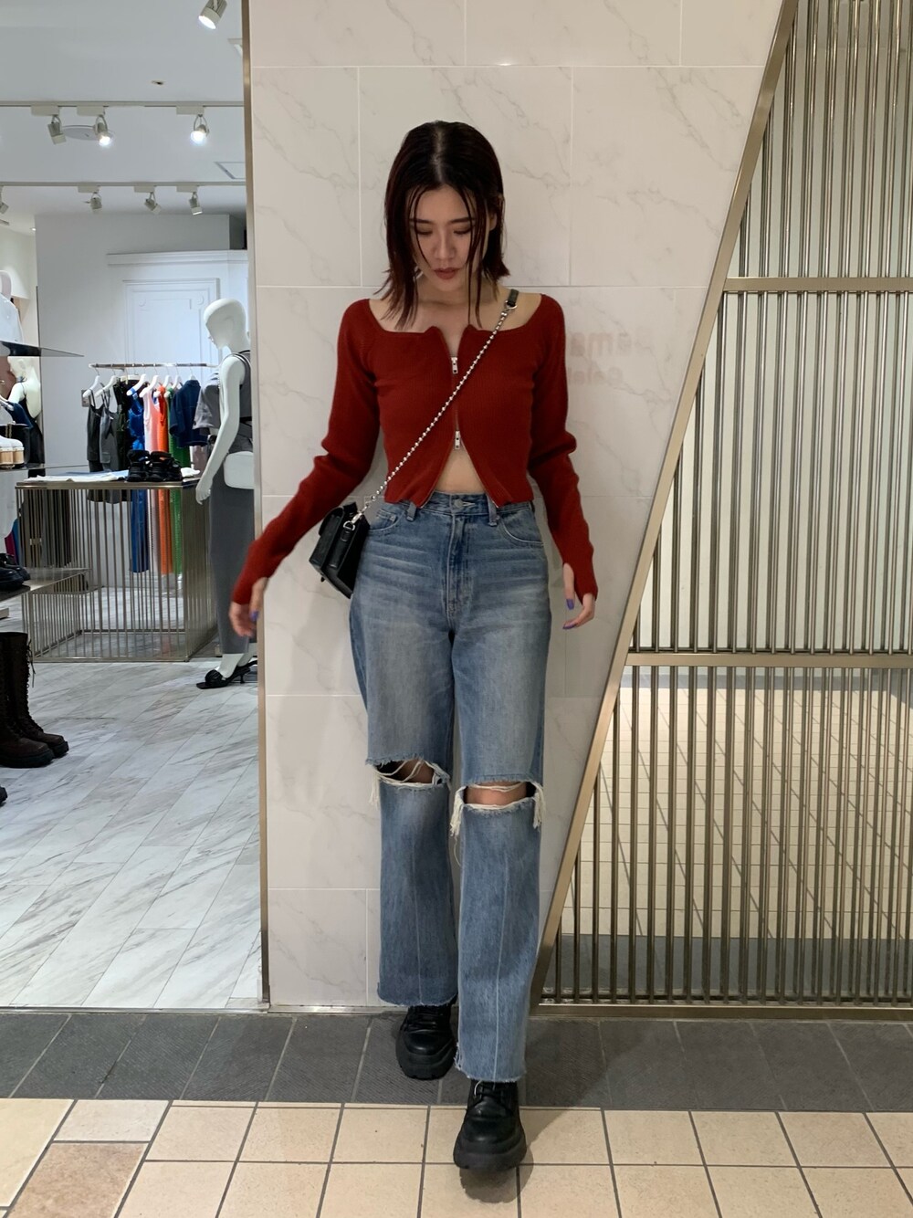 レッド系のニット/セーター、ブラック系のショルダーバッグ、ブルー系のデニムパンツを着用したレディースの夏コーディネートの1枚目の写真