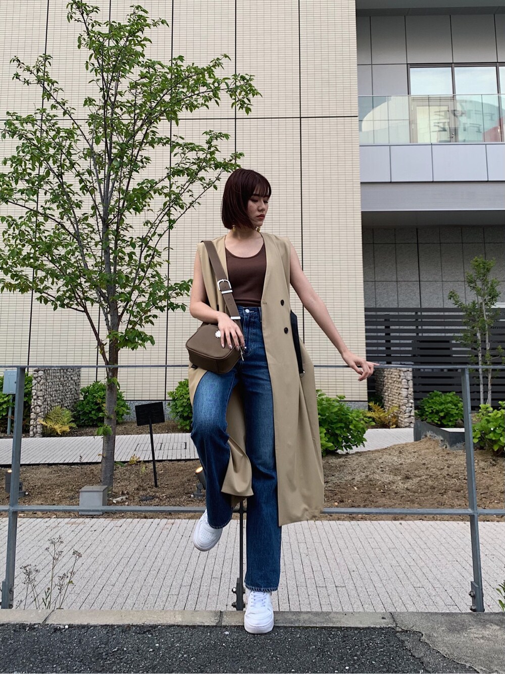 ブルー系のデニムパンツ、ベージュ系のトレンチコート、ブラウン系のタンクトップを着用したレディースの春コーディネートの1枚目の写真