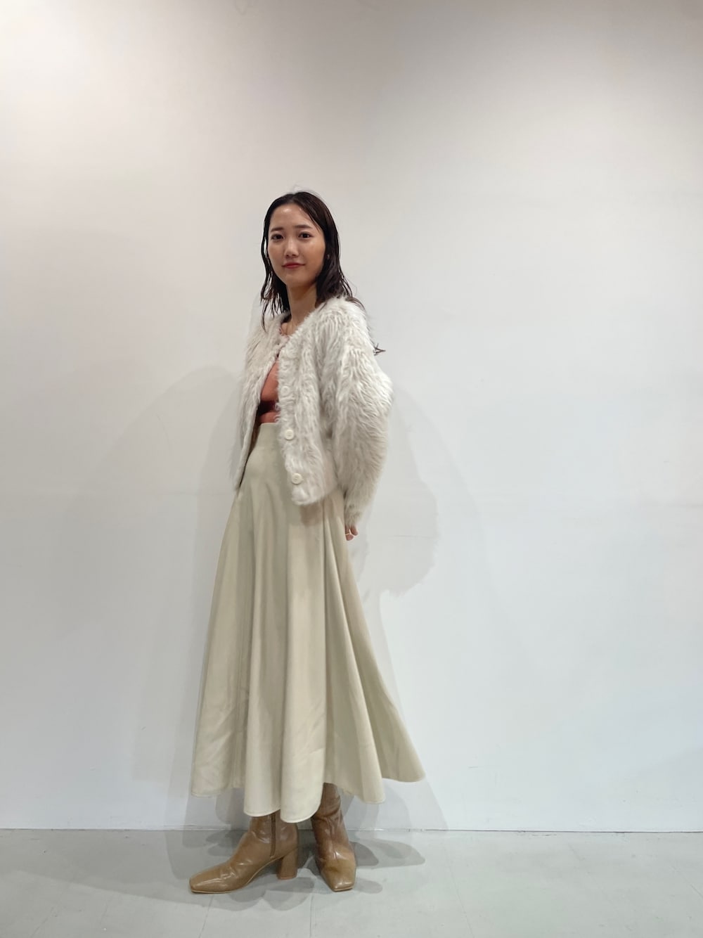 ホワイト系のスカート、ベージュ系のブーツ、オレンジ系のニット/セーターを着用したレディースの夏コーディネートの1枚目の写真