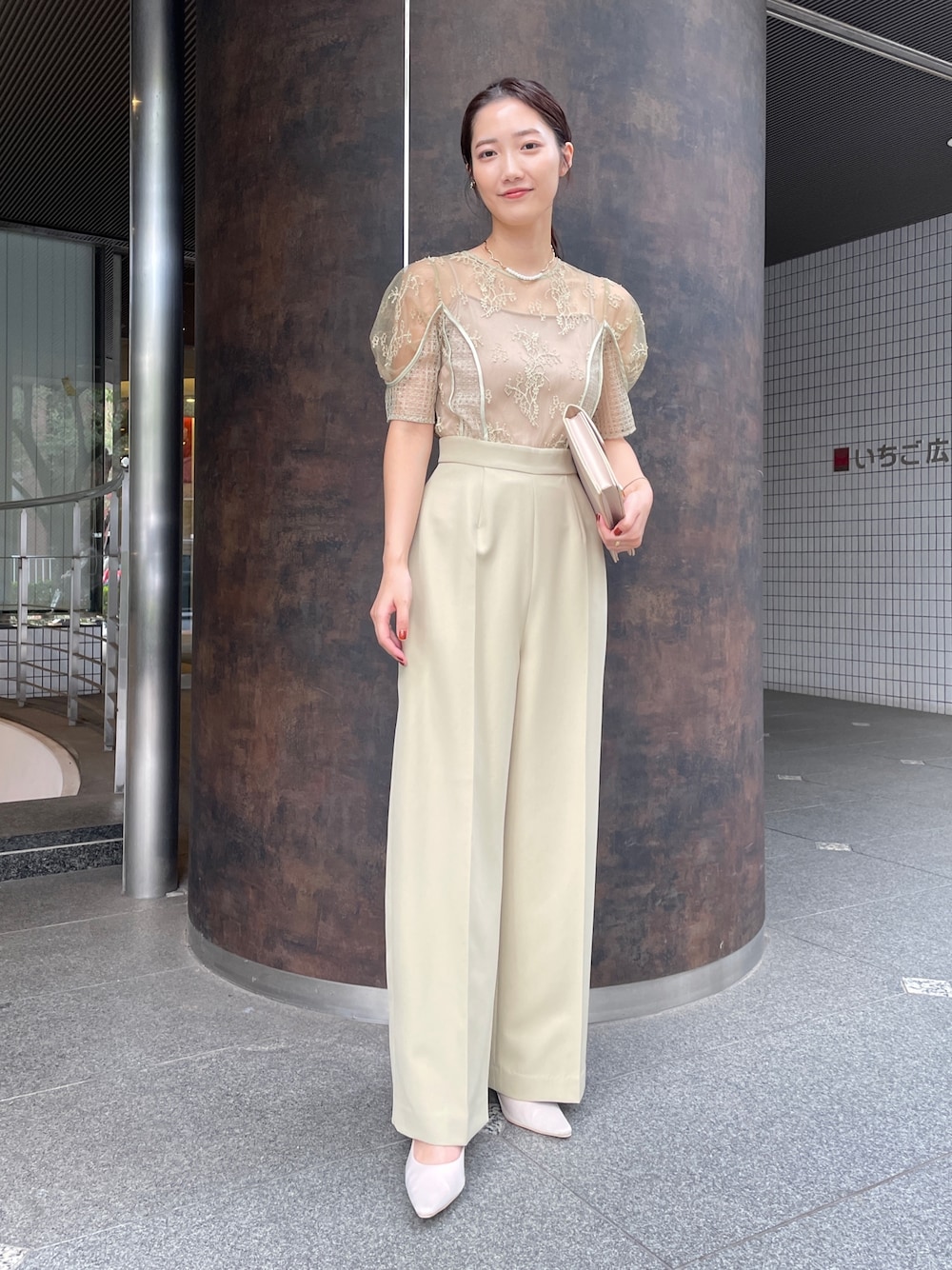 グリーン系のパンツドレス、ベージュ系のクラッチバッグ、ベージュ系のパンプスを着用したレディースの冬コーディネートの1枚目の写真