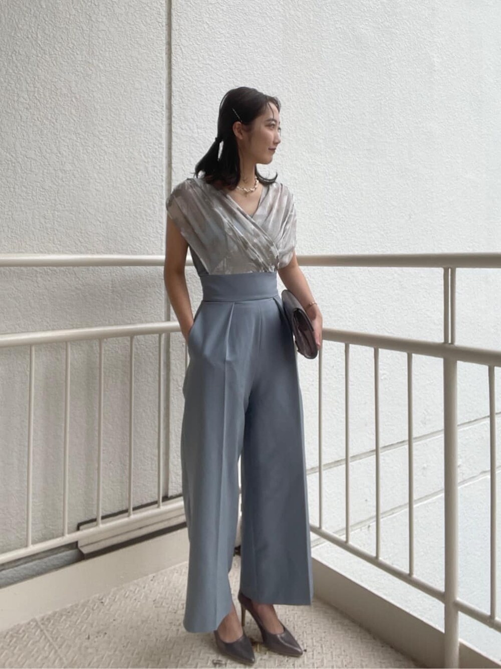 シルバー系のパンプス、シルバー系のクラッチバッグ、ブルー系のパンツドレスを着用したレディースの春コーディネートの1枚目の写真