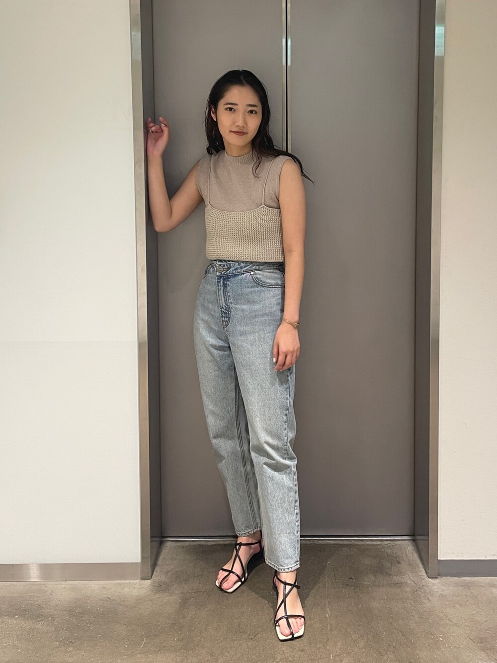 ブルー系のデニムパンツ、ベージュ系のニット/セーター、ブラック系のサンダルを着用したレディースの春コーディネートの1枚目の写真