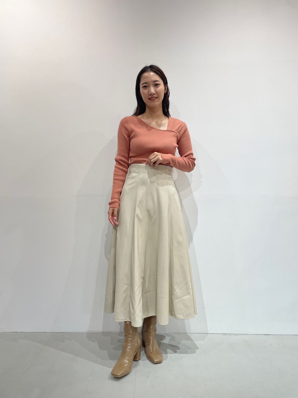 オレンジ系のニット/セーター、ホワイト系のスカート、ベージュ系のブーツを着用したレディースの夏コーディネートの1枚目の写真