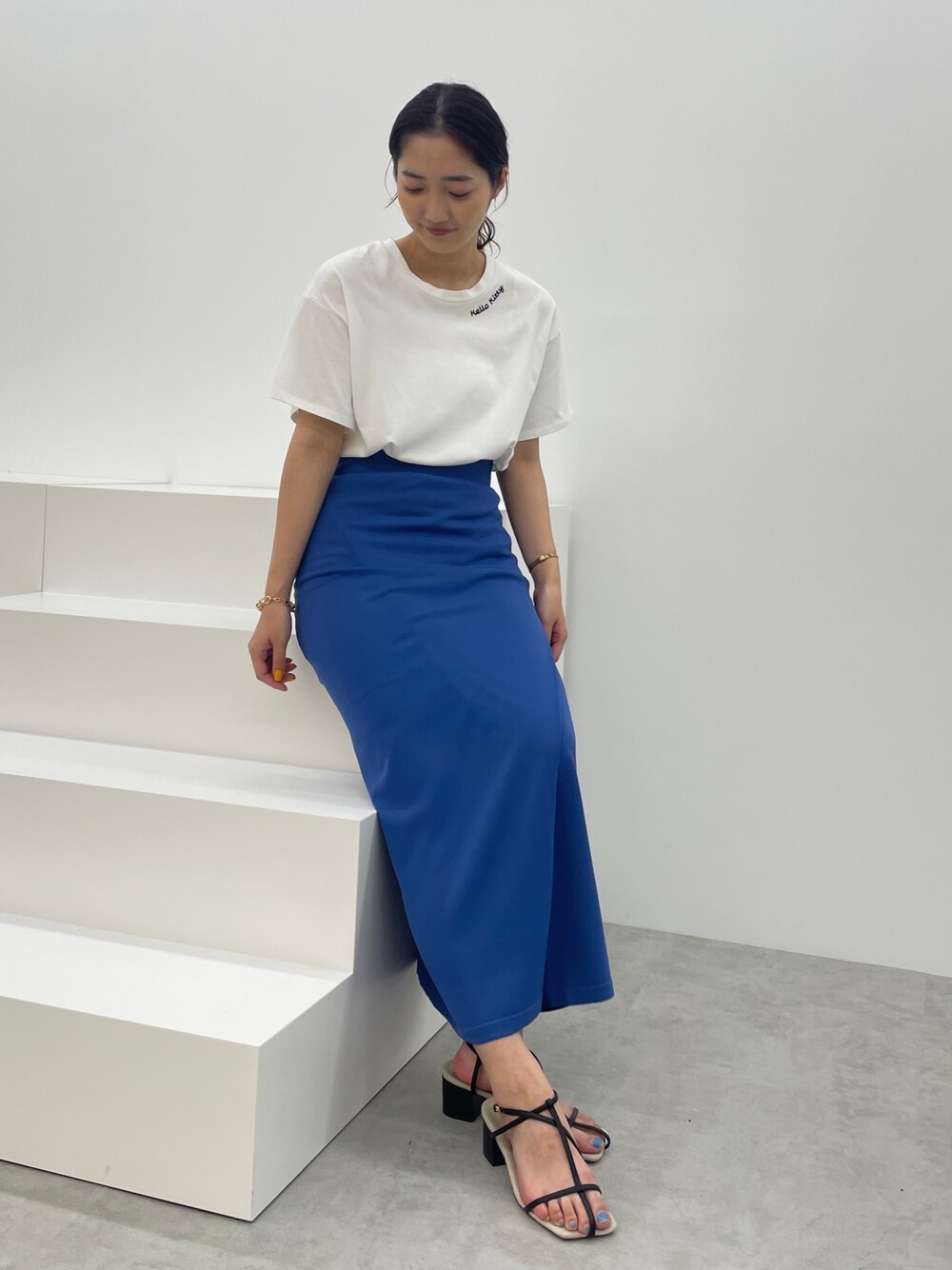 ブルー系のスカート、ホワイト系のTシャツ/カットソー、ブラック系のサンダルを着用したレディースの春コーディネートの1枚目の写真