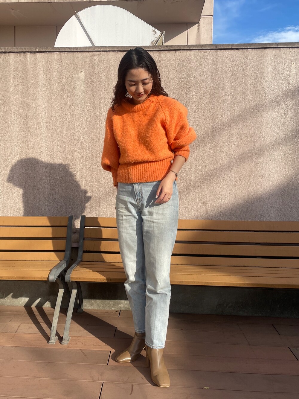 ブルー系のデニムパンツ、オレンジ系のニット/セーター、ベージュ系のブーツを着用したレディースの冬コーディネートの1枚目の写真