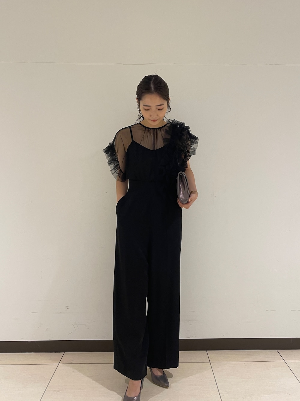ブラック系のパンツドレス、シルバー系のクラッチバッグ、シルバー系のパンプスを着用したレディースの春コーディネートの1枚目の写真