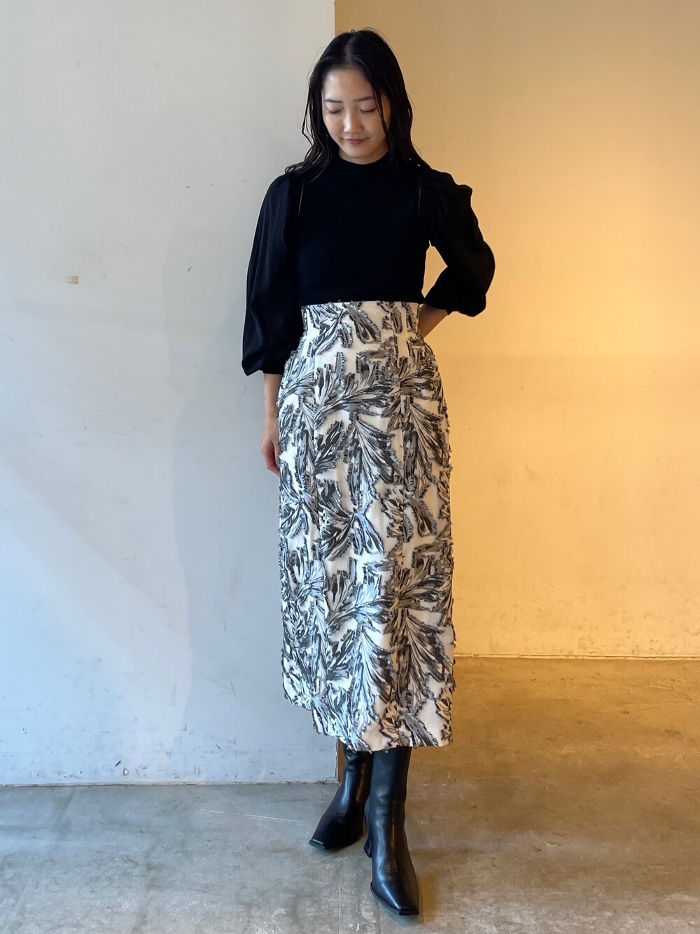 ブラック系のスカート、ブラック系のニット/セーター、ブラック系のブーツを着用したレディースの冬コーディネートの1枚目の写真