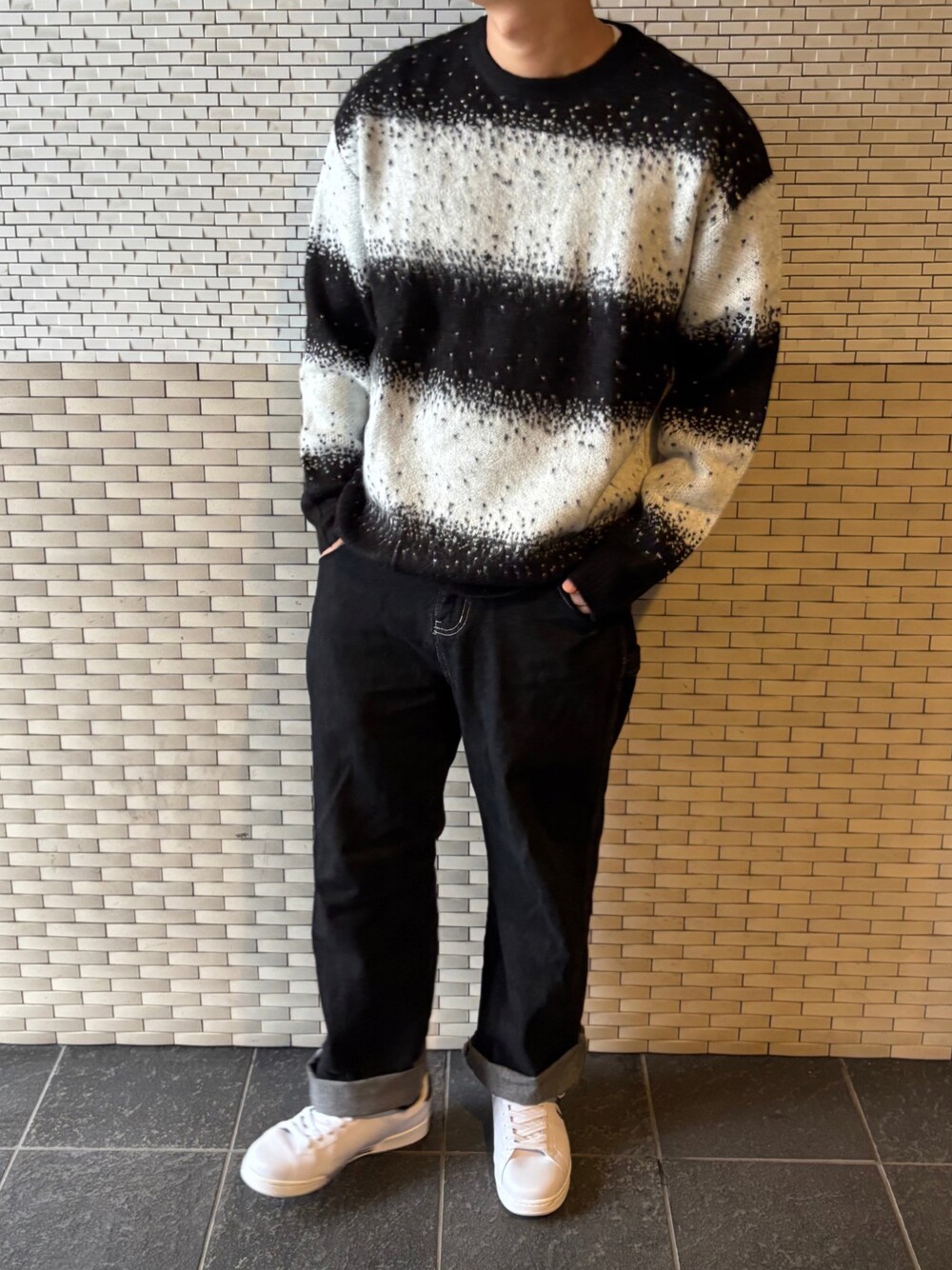 ブラック系のデニムパンツ、ブラック系のニット/セーター、ホワイト系のスニーカーを着用したメンズの秋コーディネートの1枚目の写真