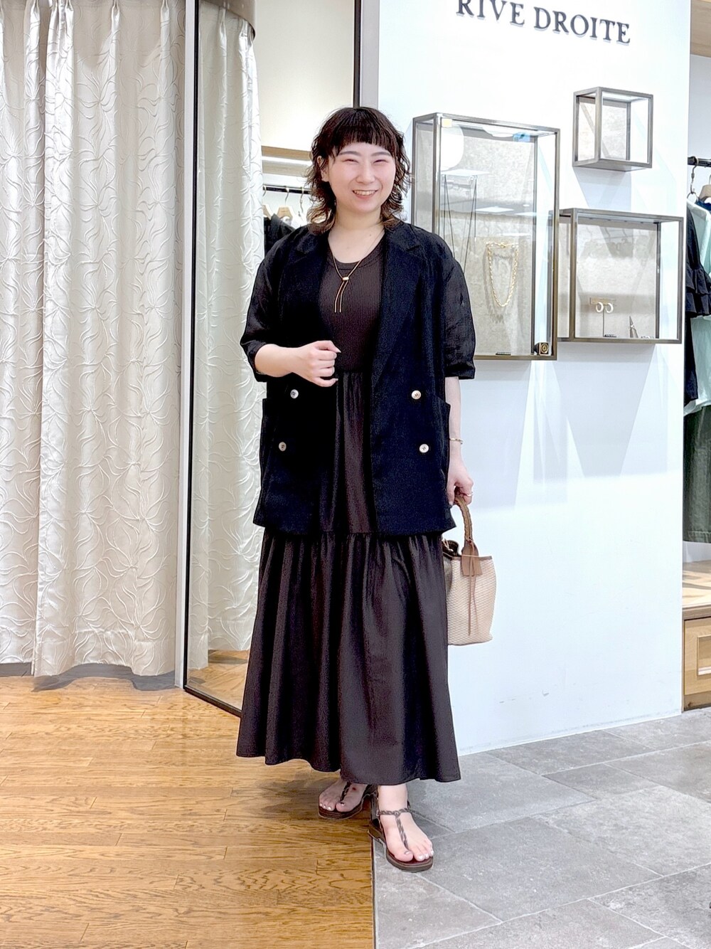 ブラック系のテーラードジャケット、ブラウン系のワンピース、ブラウン系のハンドバッグを着用したレディースの夏コーディネートの1枚目の写真