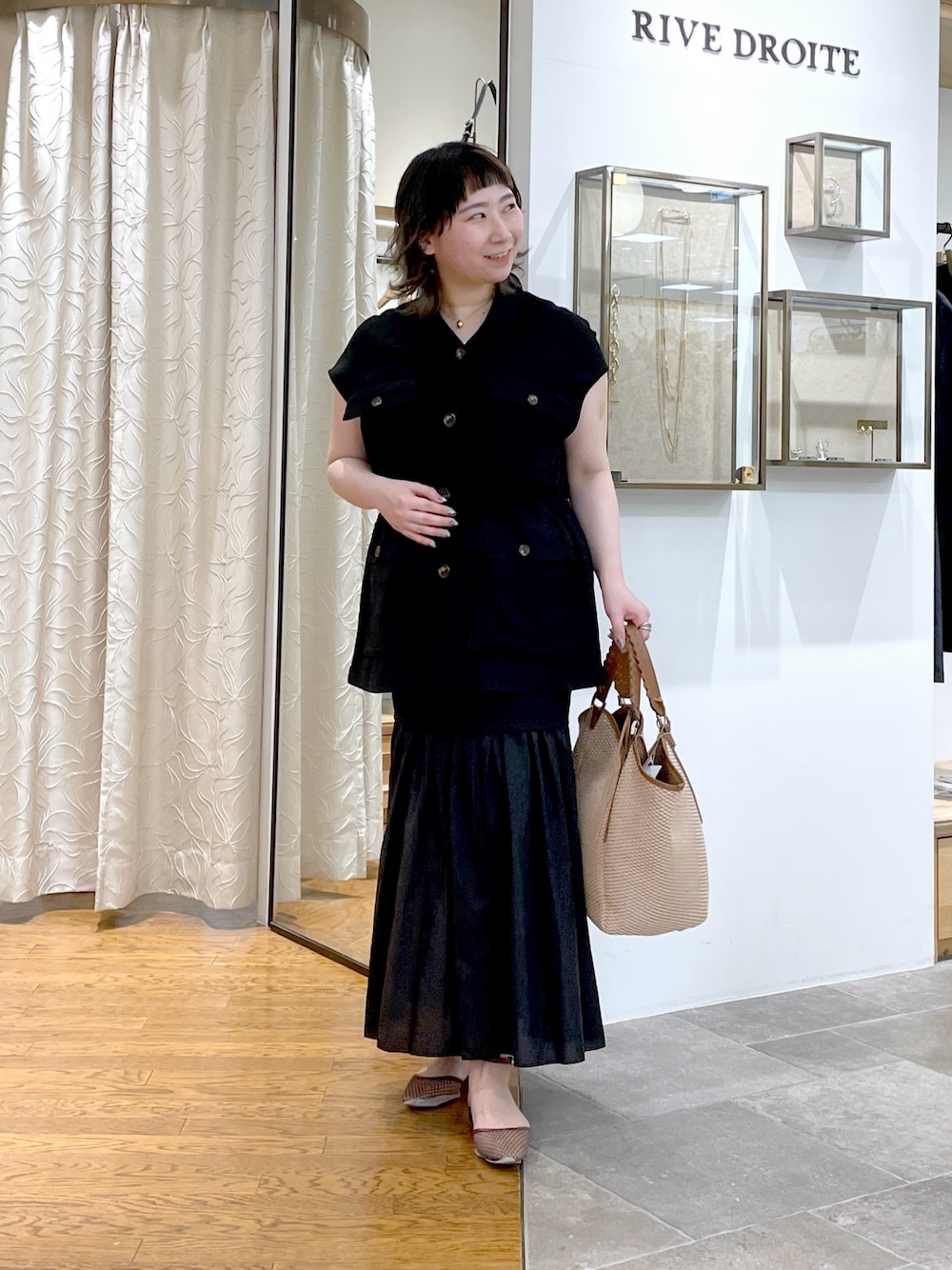 ブラック系のベスト、ブラウン系のトートバッグ、ブラック系のスカートを着用したレディースの春コーディネートの1枚目の写真