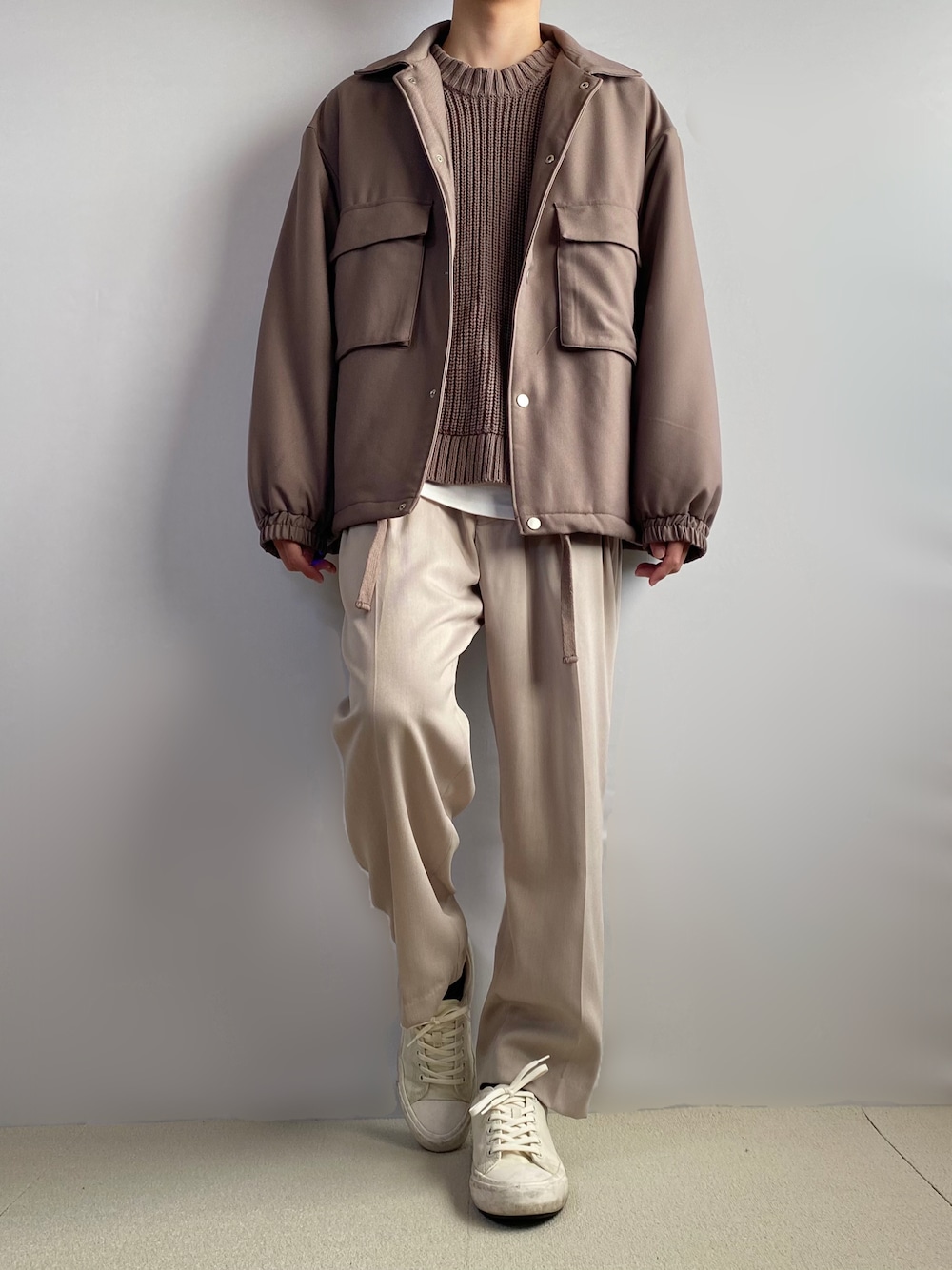 ベージュ系のスラックス、ホワイト系のスニーカー、ブラウン系のニット/セーターを着用したメンズの秋コーディネートの1枚目の写真