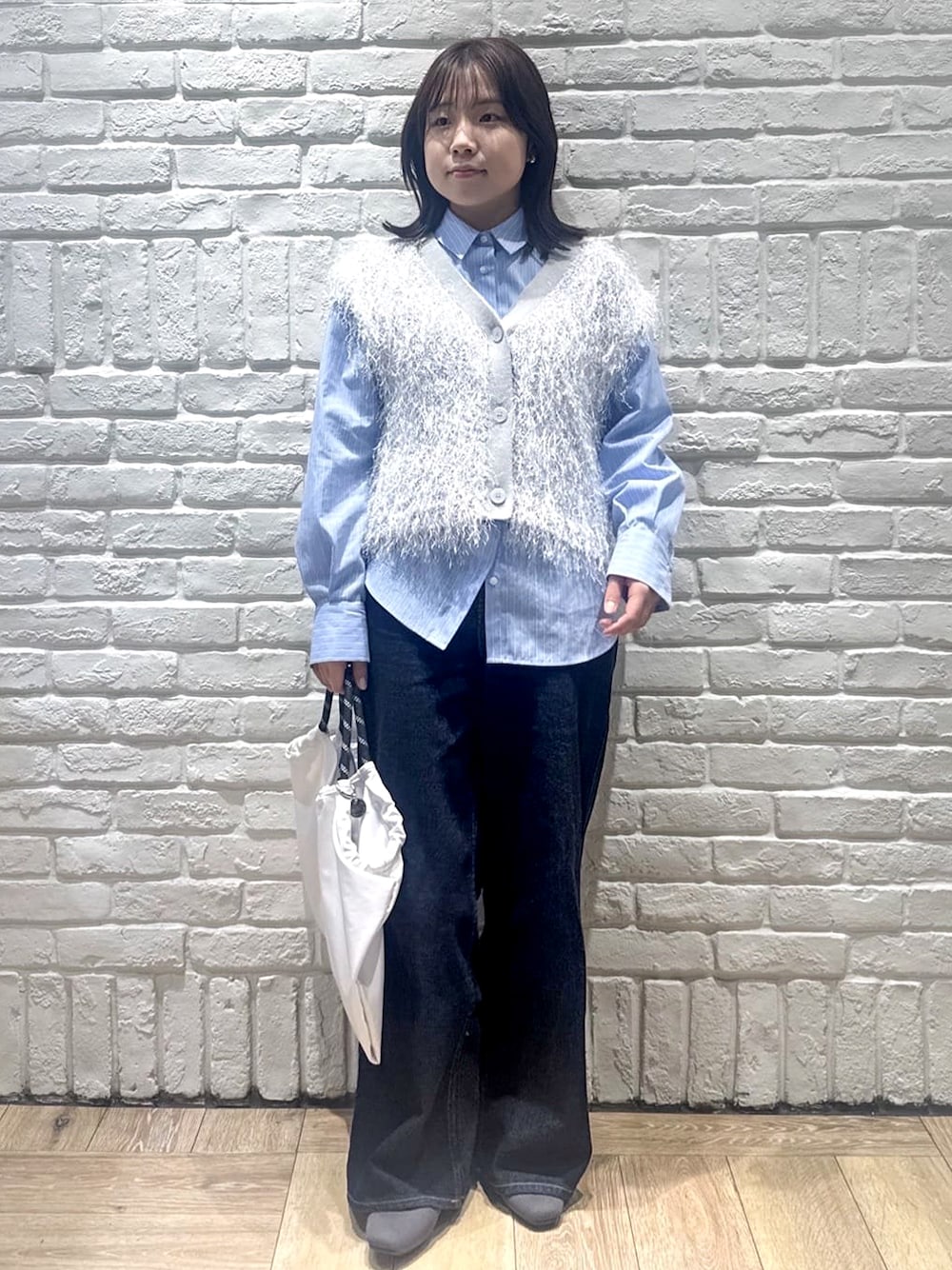 グレー系のニット/セーター、ブルー系のシャツ/ブラウス、ブルー系のデニムパンツを着用したレディースの春コーディネートの1枚目の写真
