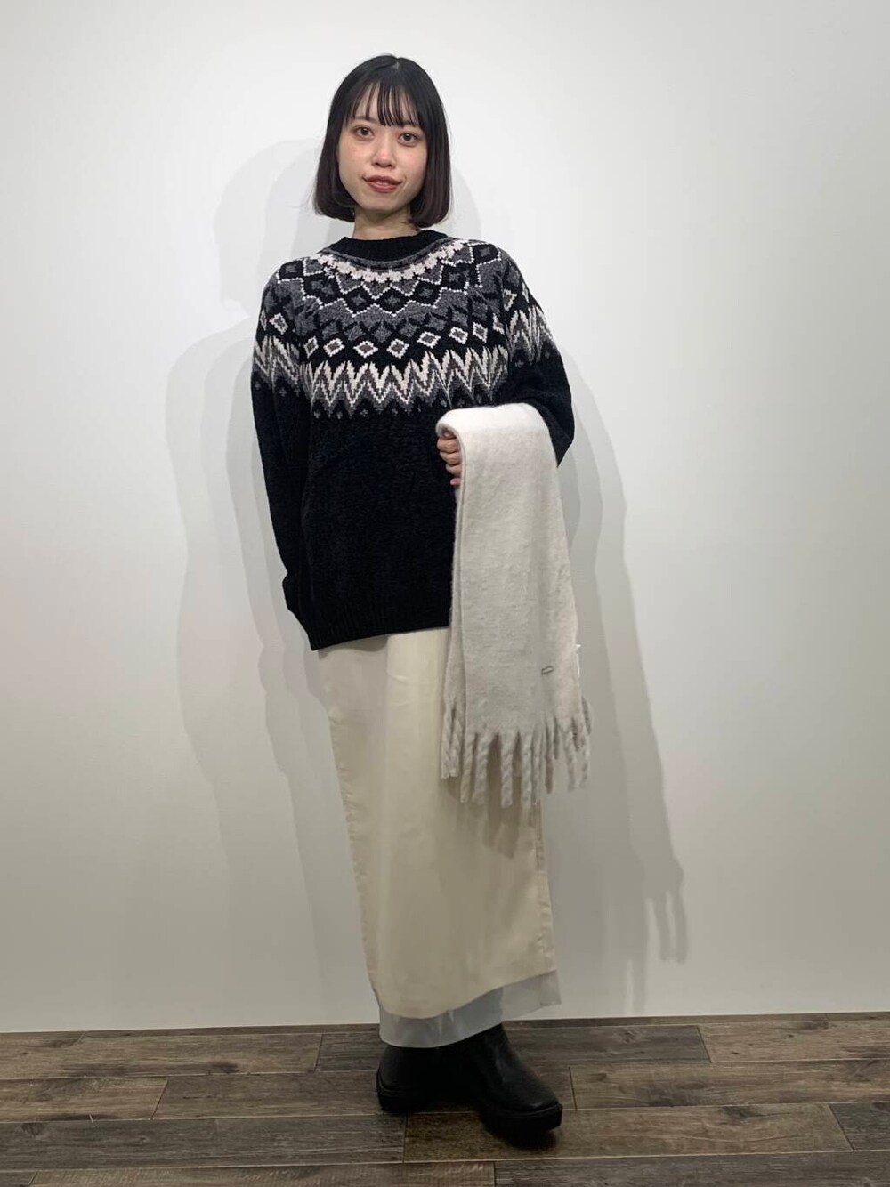 ブラック系のニット/セーター、ブラック系のブーツ、ホワイト系のスカートを着用したレディースの冬コーディネートの1枚目の写真