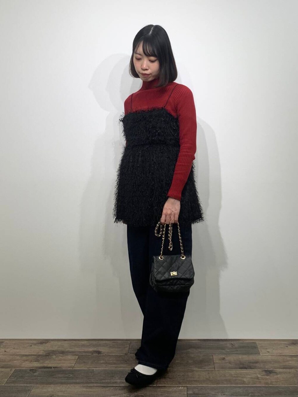 レッド系のニット/セーター、ブラック系のショルダーバッグ、ブルー系のデニムパンツを着用したレディースの冬コーディネートの1枚目の写真