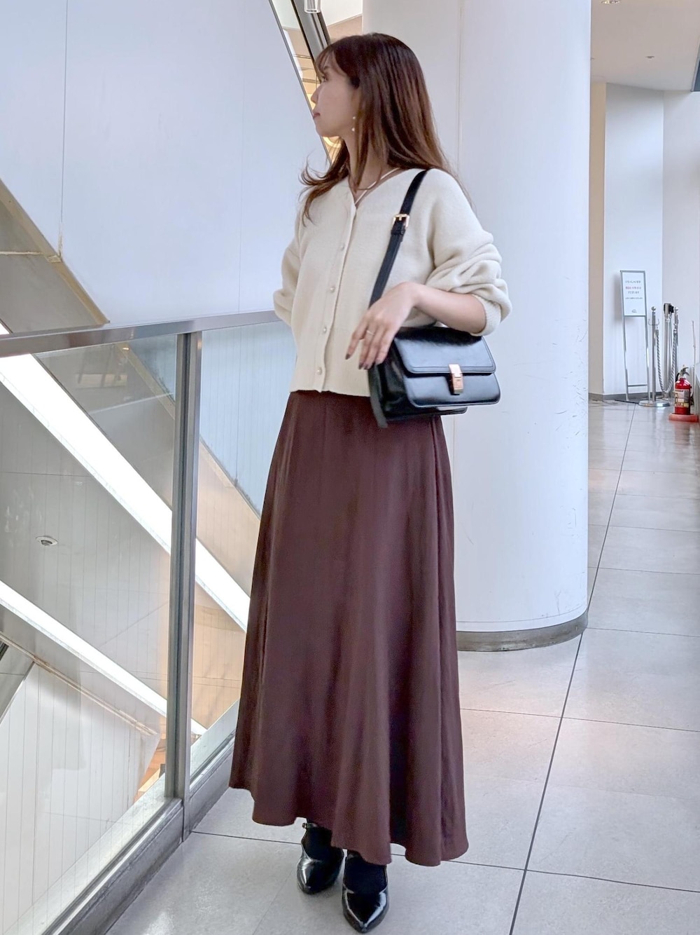 ブラック系のパンプス、ブラック系のショルダーバッグ、ホワイト系のカーディガン/ボレロを着用したレディースの秋コーディネートの1枚目の写真