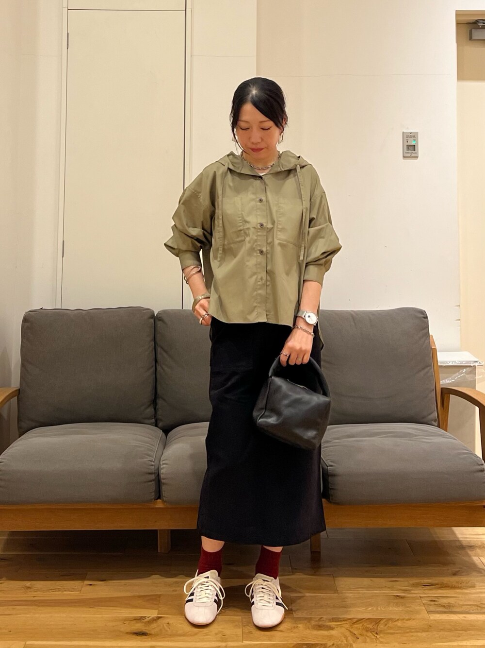 ブラック系のスカート、ブラック系のハンドバッグ、ホワイト系のスニーカーを着用したレディースの秋コーディネートの1枚目の写真