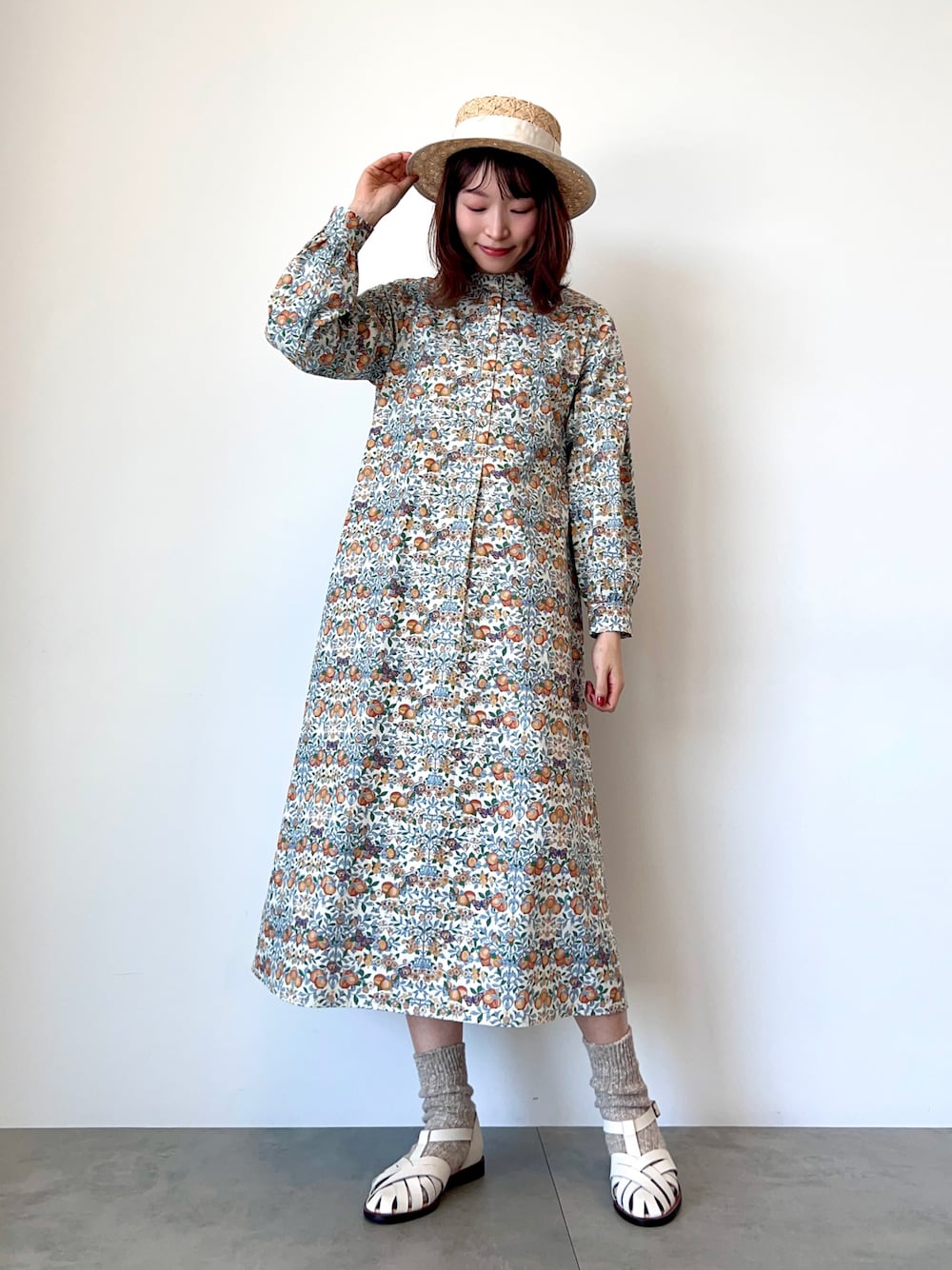 オレンジ系のワンピース、ホワイト系のサンダル、ホワイト系のハットを着用したレディースの春コーディネートの1枚目の写真