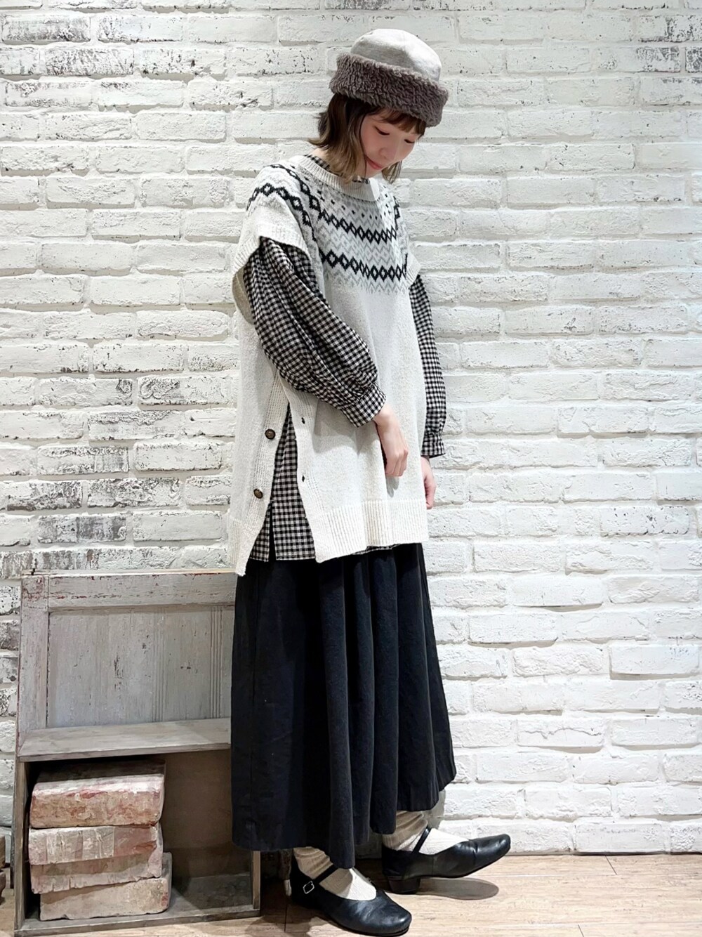 ホワイト系のベスト、ブラック系のチュニック、ブラック系のスカートを着用したレディースの冬コーディネートの1枚目の写真