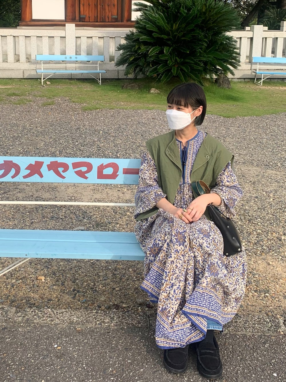 ブルー系のワンピース、グリーン系のベスト、ブラック系のハンドバッグを着用したレディースの秋コーディネートの1枚目の写真