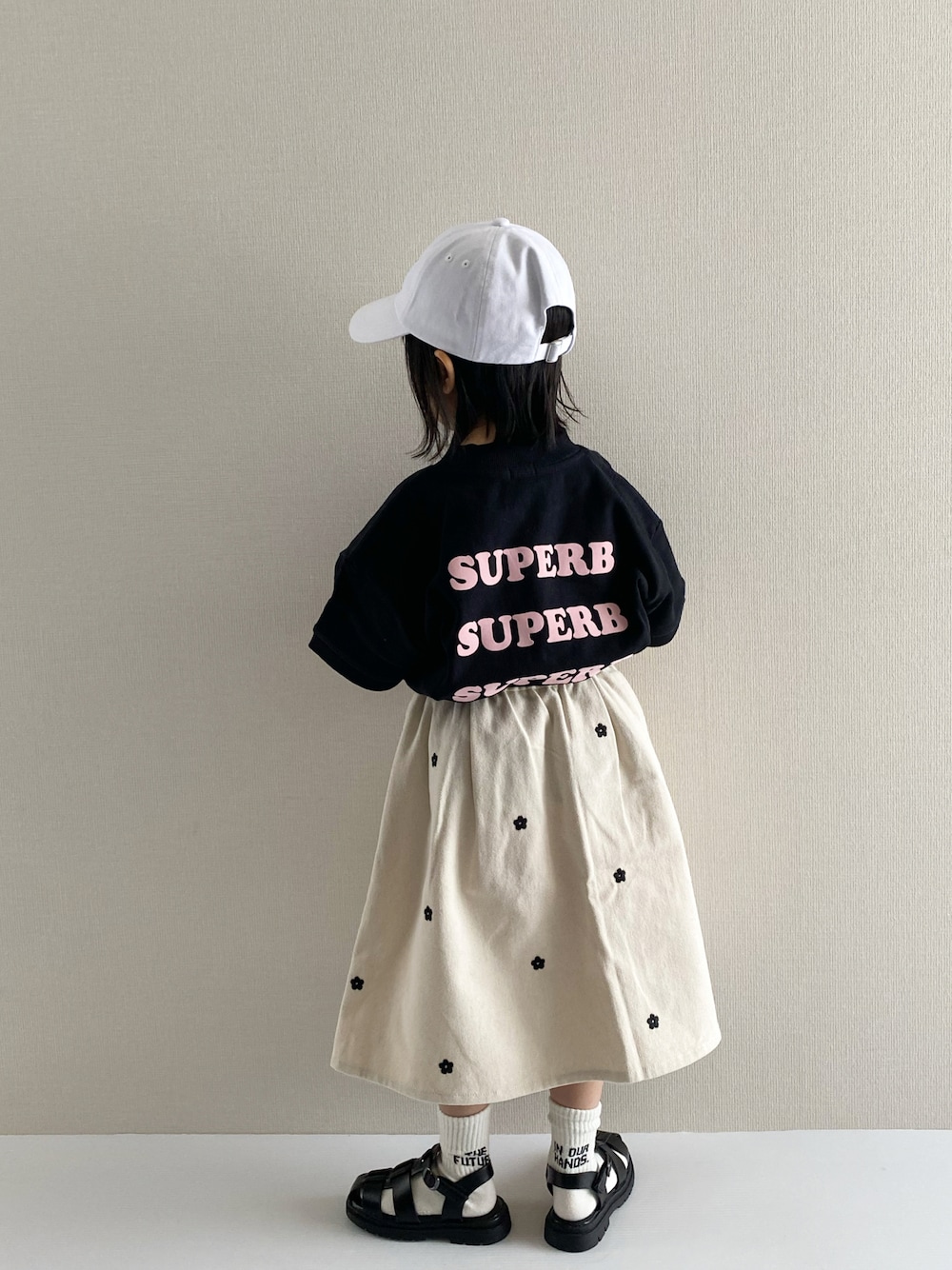 ブラック系のTシャツ/カットソー、ホワイト系のスカート、ブラック系のサンダルを着用したキッズの冬コーディネートの1枚目の写真
