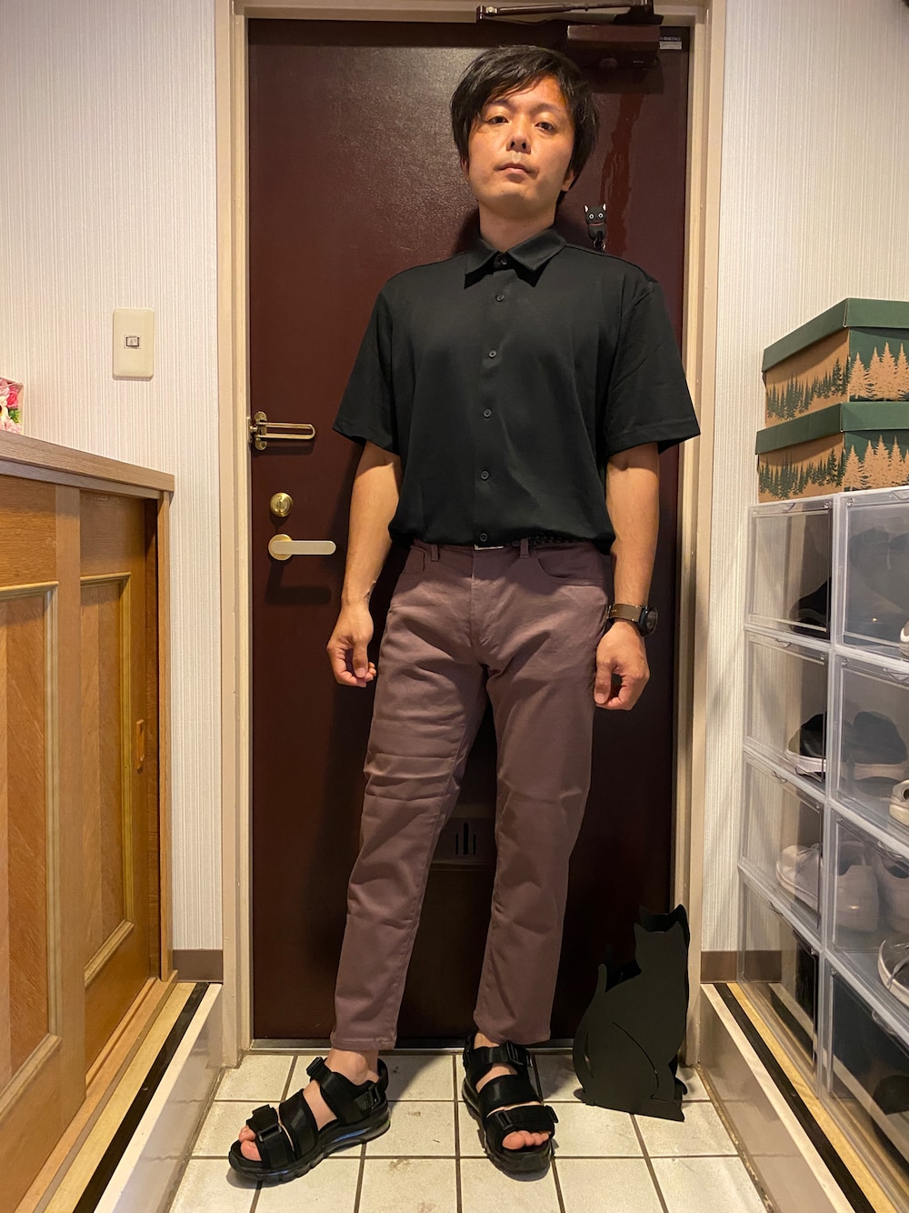 パープル系のパンツ、ブラック系のポロシャツ、ブラック系のサンダルを着用したメンズの夏コーディネートの1枚目の写真