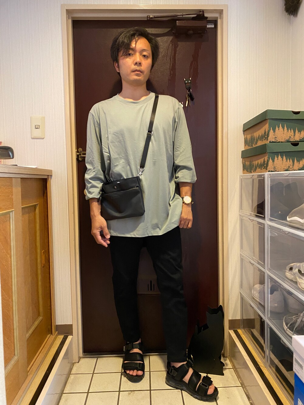 ブラック系のショルダーバッグ、グリーン系のTシャツ/カットソー、ブラック系のパンツを着用したメンズの夏コーディネートの1枚目の写真