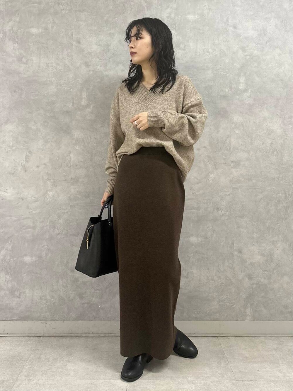 ブラウン系のスカート、ベージュ系のニット/セーター、ブラック系のトートバッグを着用したレディースの冬コーディネートの1枚目の写真