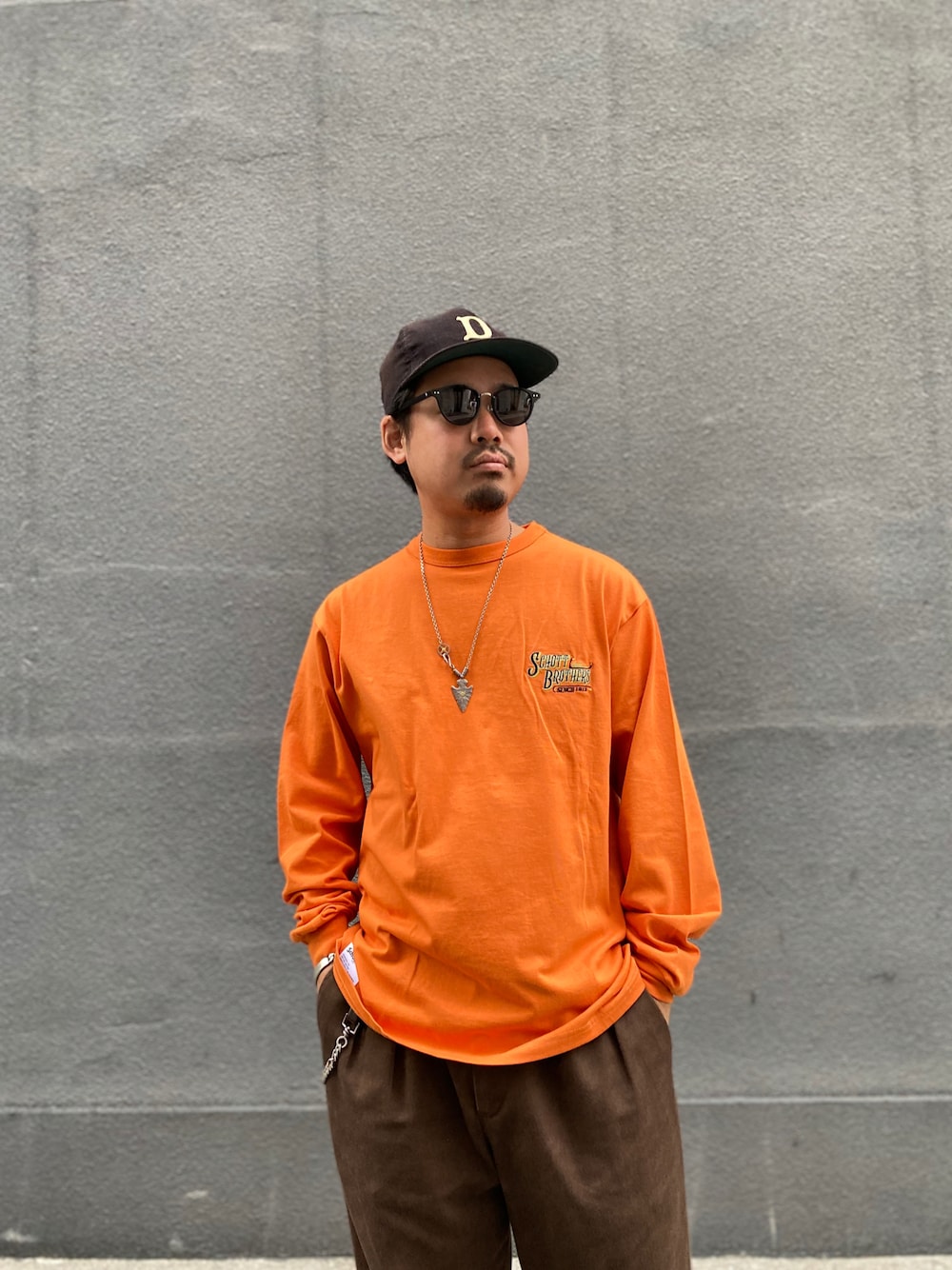 オレンジ系のTシャツ/カットソー、ブラウン系のチノパンツを着用したメンズの冬コーディネートの1枚目の写真