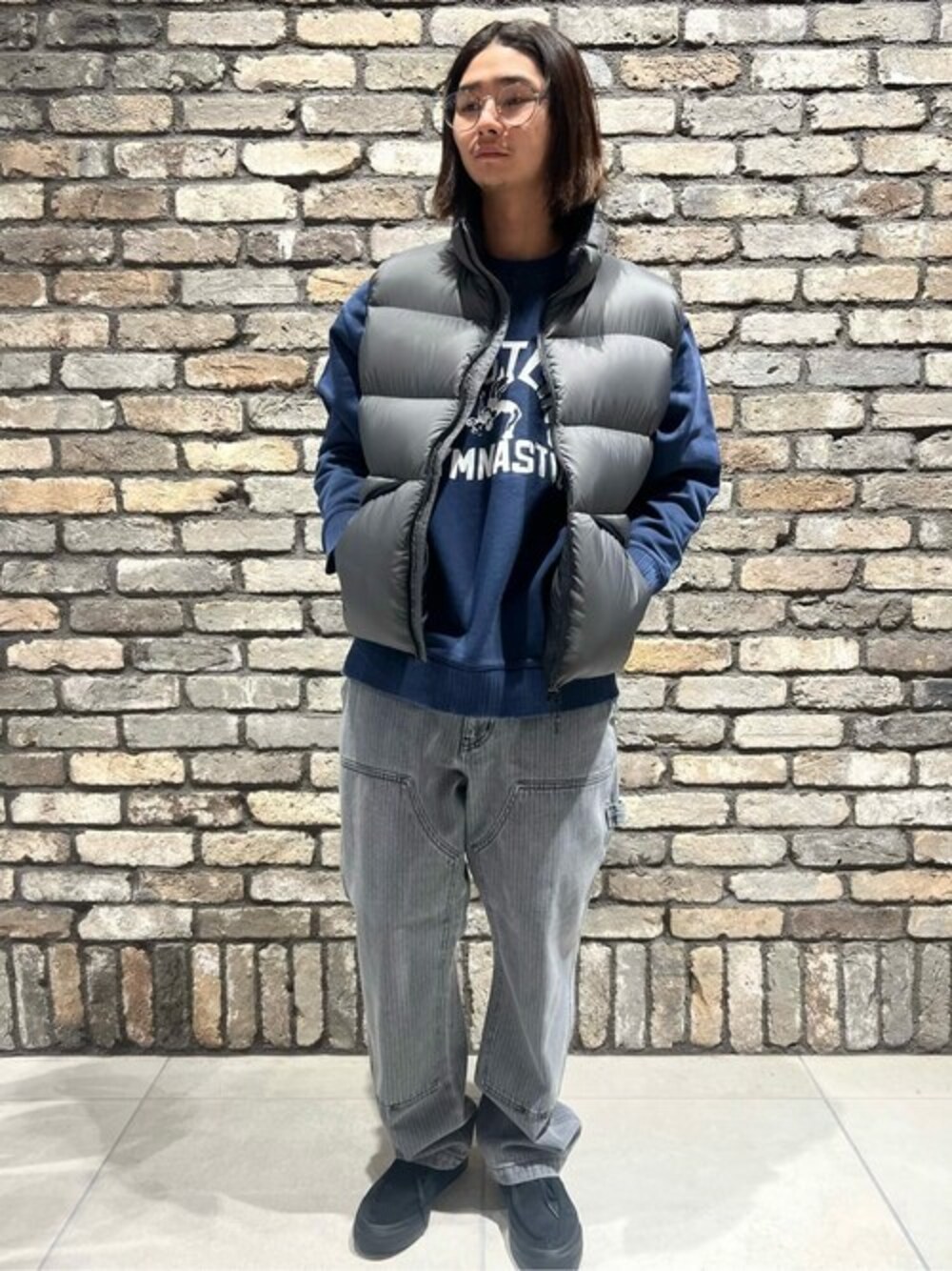 グレー系のダウンベスト、ブルー系のスウェット、ブラック系のデニムパンツを着用したメンズの冬コーディネートの1枚目の写真