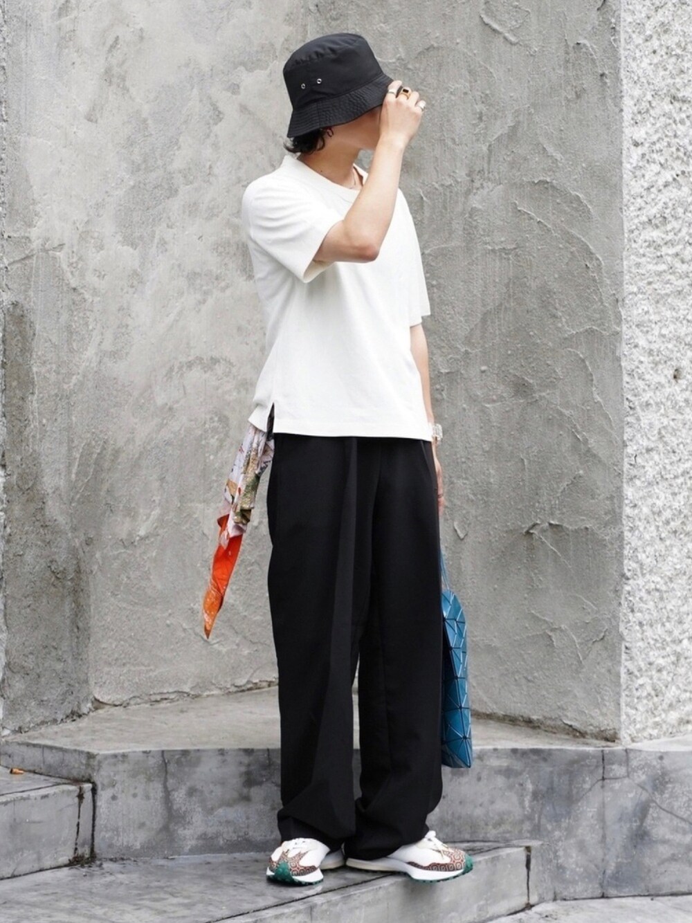 ブルー系のトートバッグ、ブラック系のスラックス、ホワイト系のTシャツ/カットソーを着用したメンズの夏コーディネートの1枚目の写真