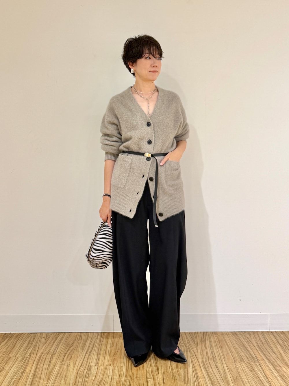 ブラウン系のカーディガン/ボレロ、ブラック系のその他パンツ、ホワイト系のクラッチバッグを着用したレディースの秋コーディネートの1枚目の写真