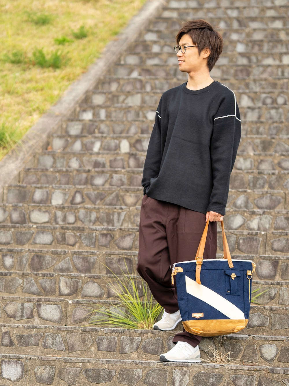 ブラック系のニット/セーター、ブラウン系のパンツ、ブルー系のトートバッグを着用したメンズの秋コーディネートの1枚目の写真