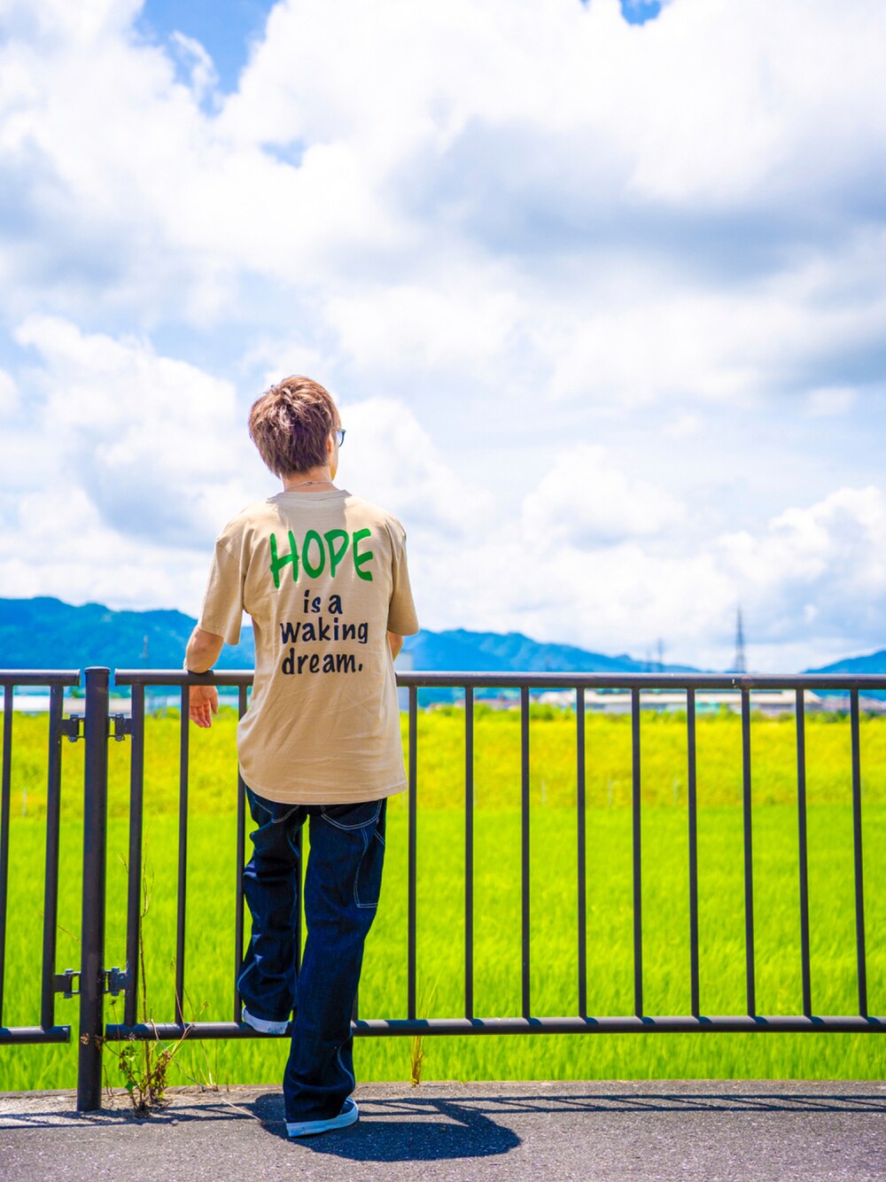 ベージュ系のTシャツ/カットソー、ブルー系のデニムパンツ、ブラック系のスニーカーを着用したメンズの夏コーディネートの1枚目の写真