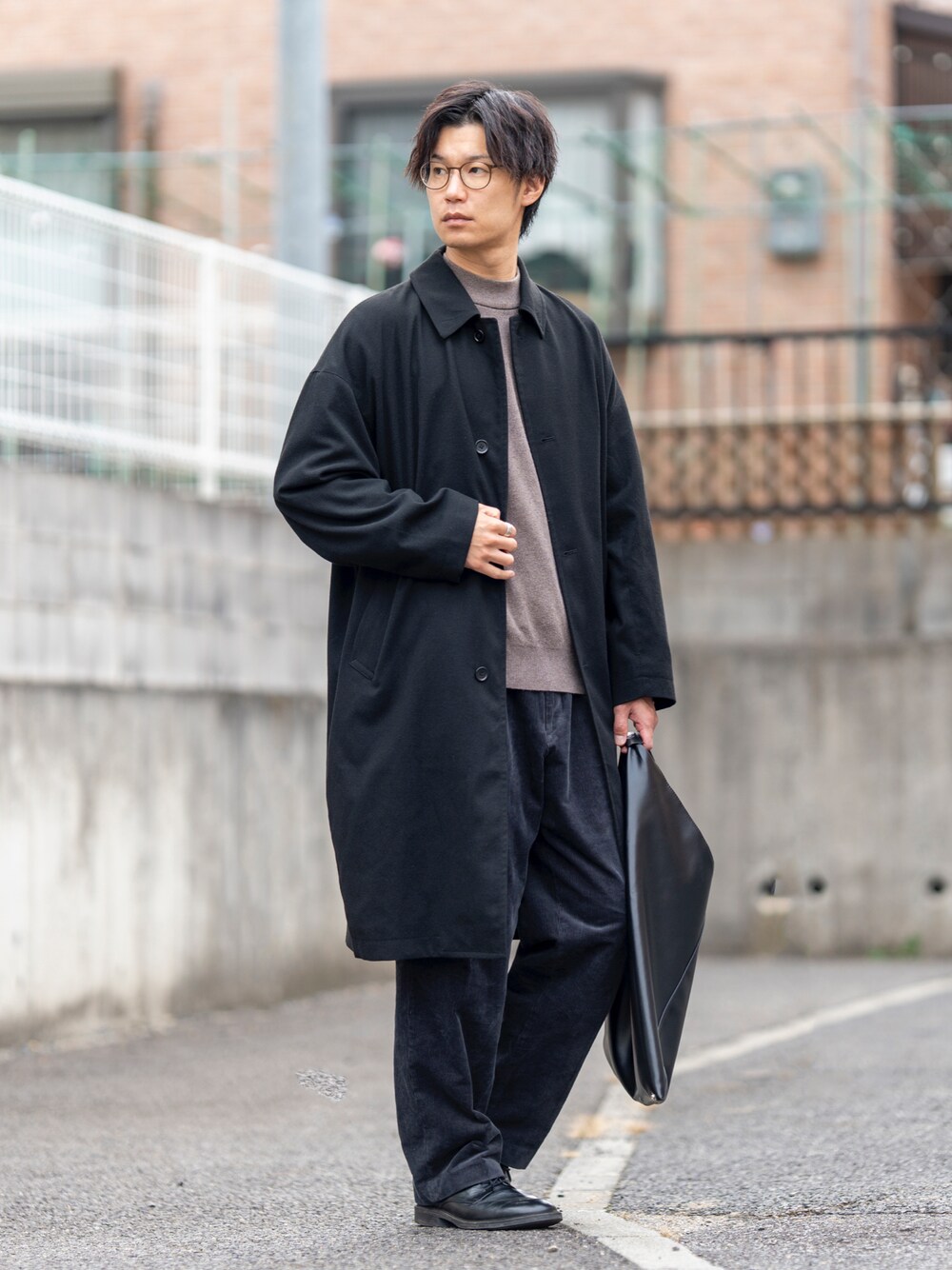 ブラック系のステンカラーコート、ブラウン系のニット/セーター、グレー系のパンツを着用したメンズの冬コーディネートの1枚目の写真