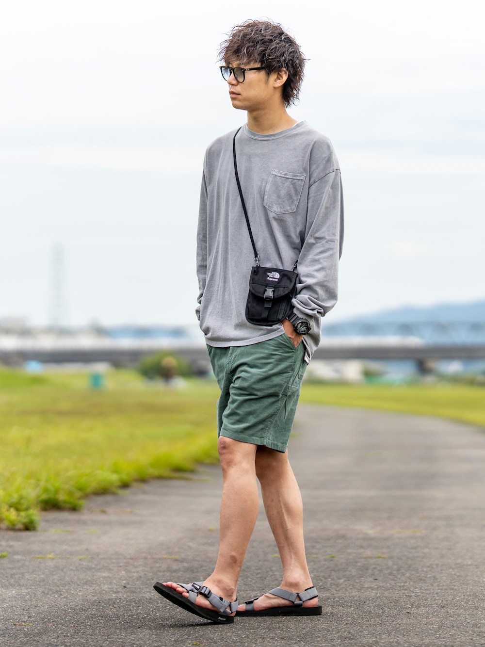 グレー系のTシャツ/カットソー、ブラック系のショルダーバッグ、グリーン系のパンツを着用したメンズの夏コーディネートの1枚目の写真