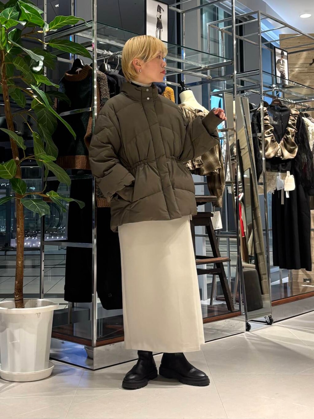 グリーン系のダウンジャケット/コート、ブラック系のニット/セーター、ベージュ系のスカートを着用したレディースの秋コーディネートの1枚目の写真